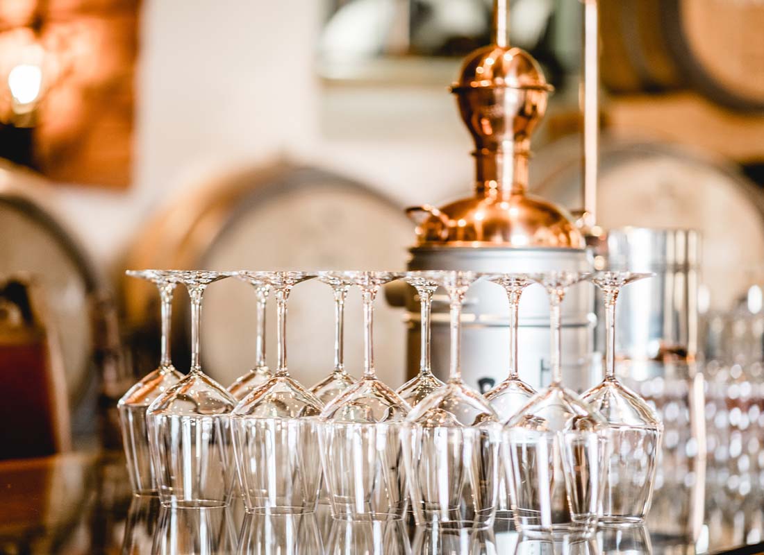 Distillery Insurance - Close-up of an Glassware and an Alembic Still Used for Making Alcohol inside a Distillery with Whisky Barrels in the Background